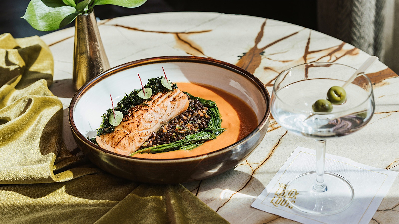 A dish of salmon next to a Martini cocktail at Louix Louis